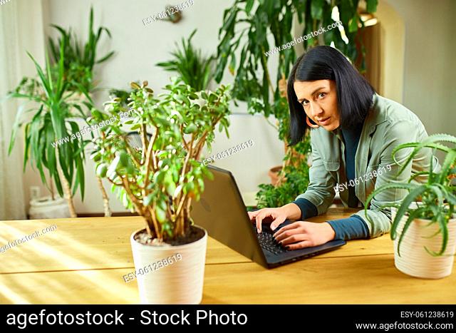 Woman browsing information about houseplant, female use laptop, Home gardening, Hobbies and leisure, Concept of home garden, green home Biophilia design