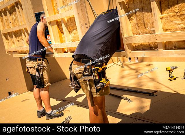 germany, bavaria, construction of a prefabricated wooden house, installation of a partition wall, carpenter with tool belt