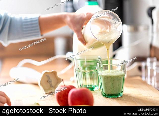 Woman pouring smoothie in glass on kitchen counter