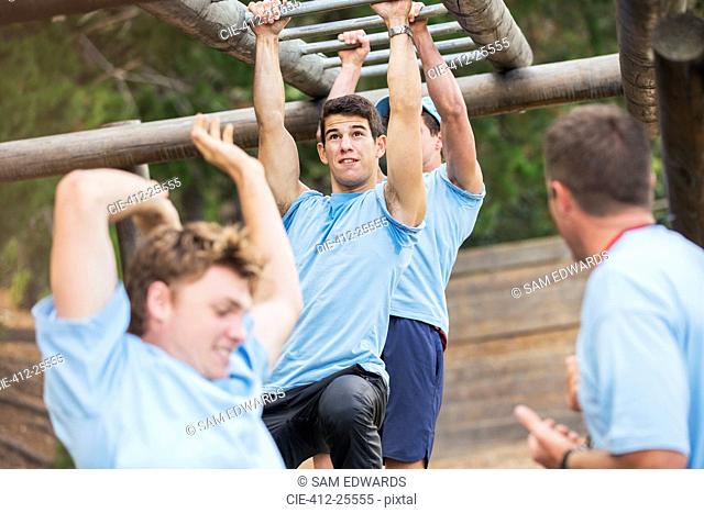 Determined man swinging on monkey bars on boot camp obstacle course