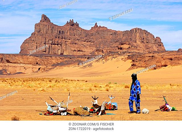 Tuareg neben den Sätteln seiner Reitkamele auf einem Rastplatz in der Wüste, Sahara, Libyen / Tuareg nomad placed next to the saddles of his Mehari dromedaries...