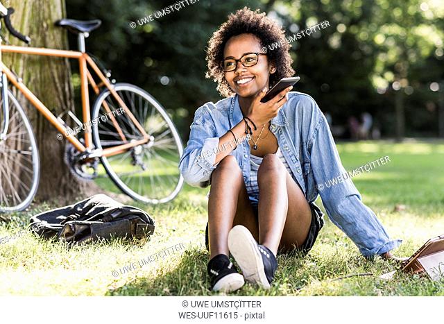 Smiling young woman resting in park with cell phone and tablet