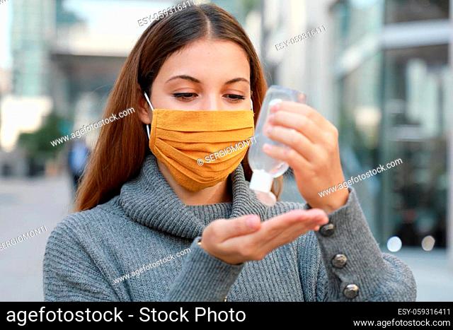 Close up of young woman with protective mask using alcohol gel sanitizer hands in modern city street