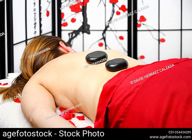 Stone treatment. Young woman lying on front enjoying a massage at spa with hot stones on her back. Beauty treatment concept