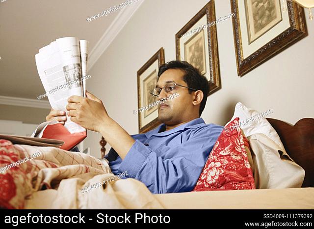 Indian man reading newspaper in bed