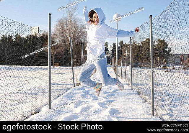 Carefree woman with arms outstretched smiling while jumping by fence