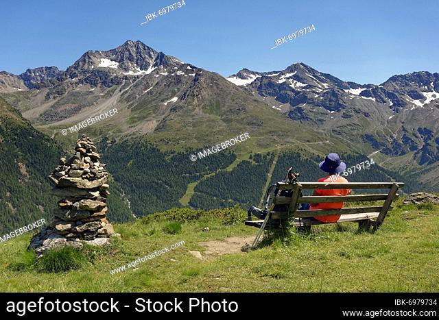 Next to cairn, woman looking at bench near Restaurant Langenstein, K2, into the Suldental valley at Vertainspitze, Schildspitze