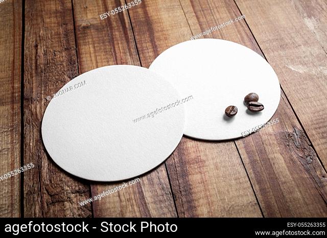 Two blank white beer coasters and coffee beans on wooden background. Responsive design mockup