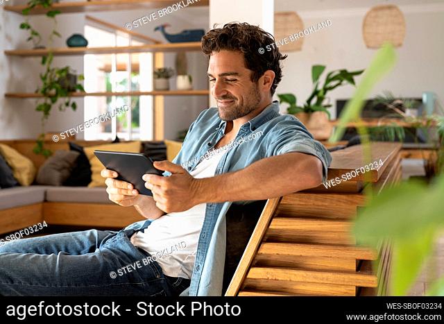 Smiling mid adult man looking at digital tablet while sitting on couch at home