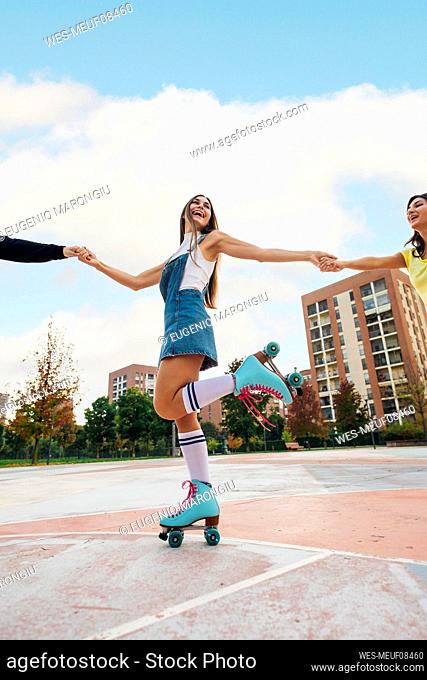 Happy woman holding hands of friends and roller skating at sports court
