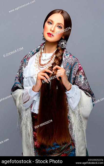Beautiful young russian woman with very long braid in traditional shawl. Red lips. Over grey background