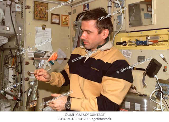 Cosmonaut Yuri I. Malenchenko, Expedition 7 mission commander, is pictured holding a spoon while a package of food floats nearby in the Zvezda Service Module on...