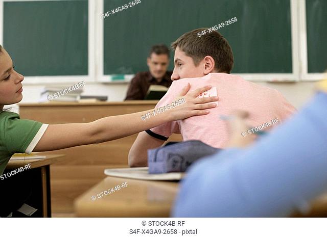 Teenage girl putting a slip of paper on schoolmate's back