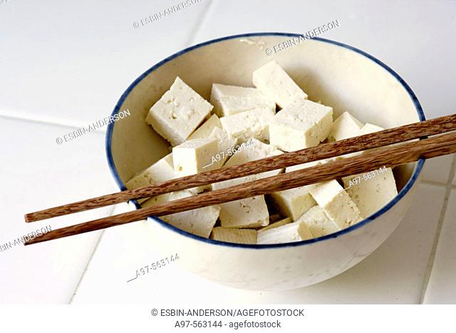 Pieces of Tofu cut into cubes and sitting in a bowl with a pair of chopsticks resting on top