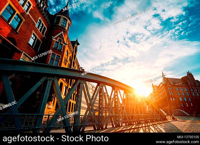 Metal arch bridge and old red bricks building in the Speicherstadt warehouse district of Hamburg HafenCity with sunburst light during sunset golden hour and...
