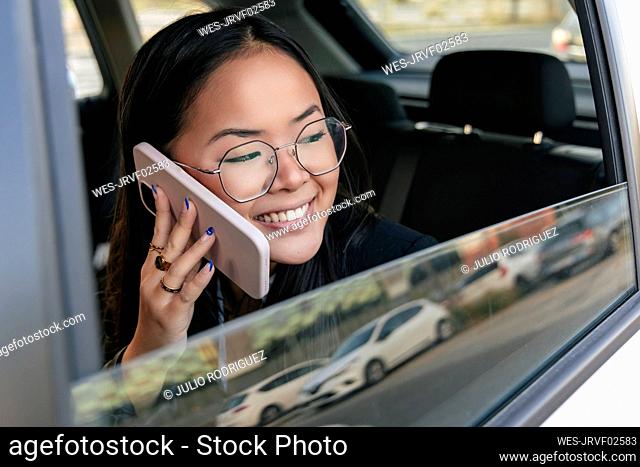 Smiling businesswoman looking out of car window talking on smart phone