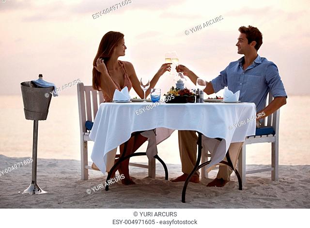 Portrait of an attractive young couple toasting champagne and enjoying dinner in beach
