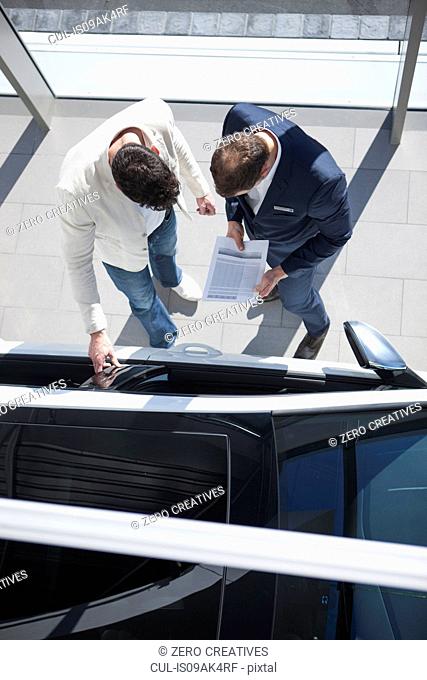 Overhead view of salesman and customer looking at new car in car dealership