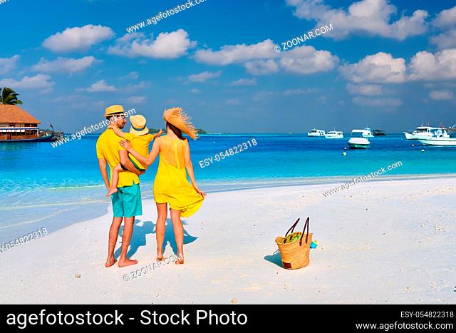 Family on beach, young couple in yellow with three year old boy. Summer vacation at Maldives
