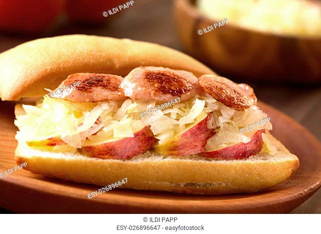 Apple, sauerkraut and bratwurst sandwich on wooden plate, photographed with natural light (Selective Focus, Focus on the front of the bratwurst slices)
