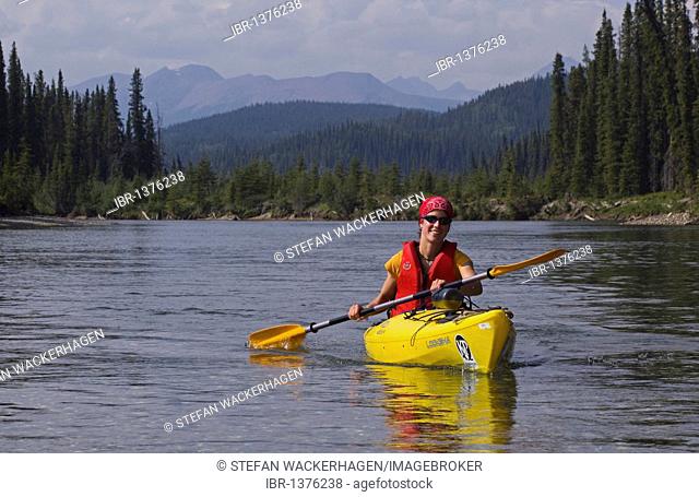 Young woman paddling a kayak, kayaking, upper Liard River, Pelly Mountains behind, Yukon Territory, Canada