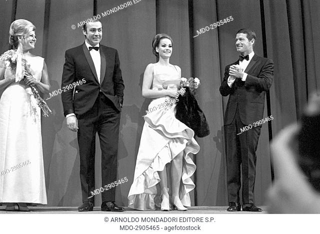 British actors Sean Connery and Stephen Boyd standing on the stage of a cinema award ceremony between two women holding bunches of flowers