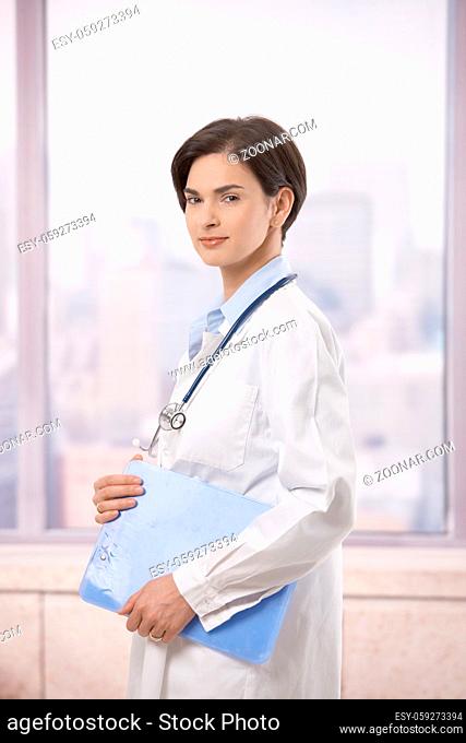 Portrait of attractive female doctor walking on hospital corridor, smiling at camera