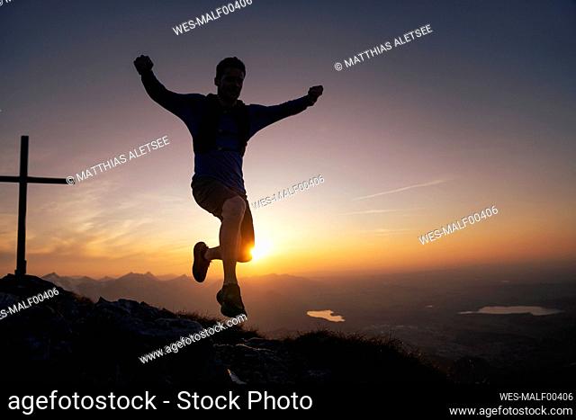 Hiker jumping on mountain peak at sunset