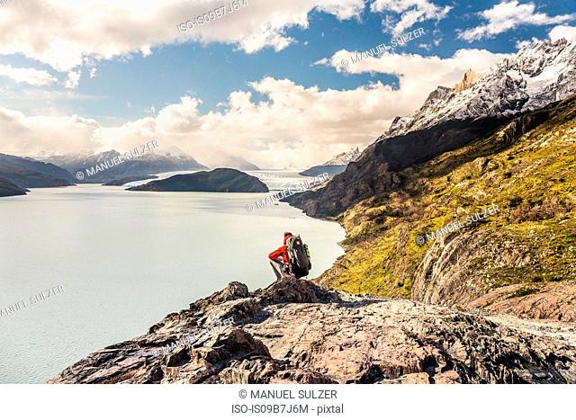 Male hiker crouching to look out over Grey Lake and Glacier, Torres del Paine national park, Chile