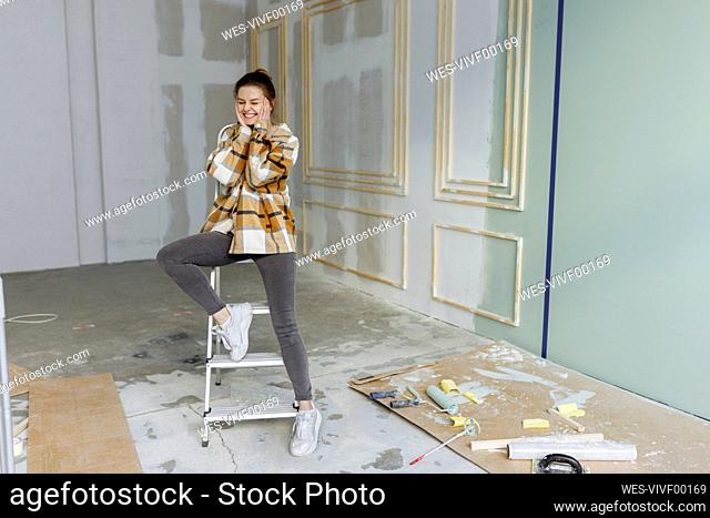 Happy young woman with head in hands leaning on ladder at home