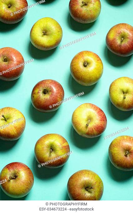 A selection of cox's orange pippin apple laid out in rows on a blue green background shot from above with soft shadows