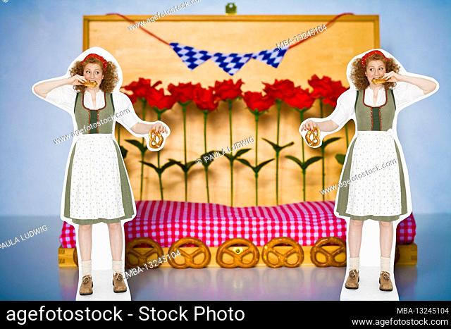 Still-life photo, 2 women in dirndls, with pretzels in their hands, biting into a pretzel, standing in front of a wooden decoration, with pretzels