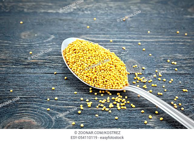 Mustard seeds in a metal spoon on the background of a wooden board
