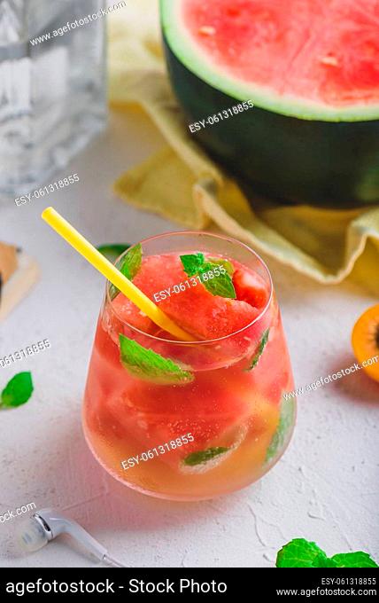 Fresh watermelon cocktail with gin and sparkling water, garnished with mint leaves and yellow straw in glass on light concrete background