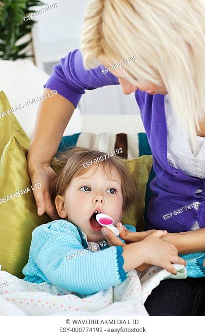 Sick little girl getting syrup from her caring mother at home