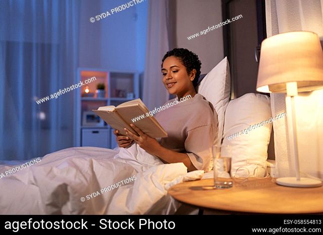 smiling young woman reading book in bed at home
