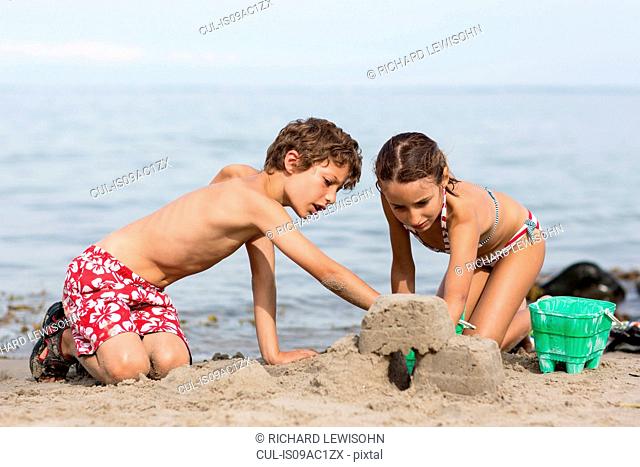 Brother and sister on beach building sandcastle
