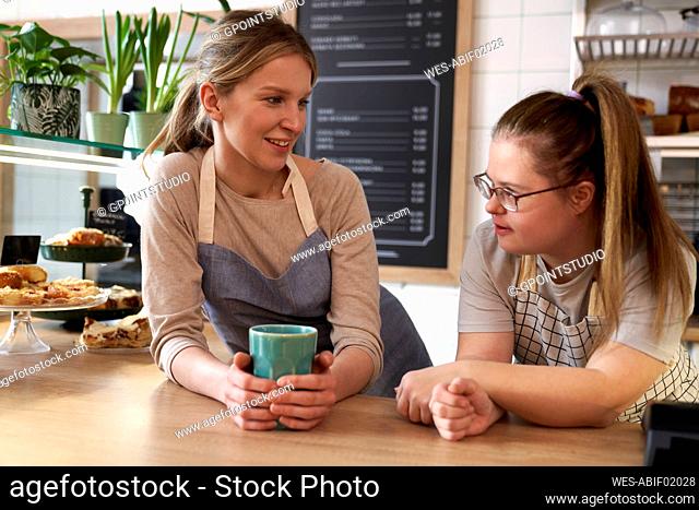 Smiling cafe owner with down syndrome talking to colleague
