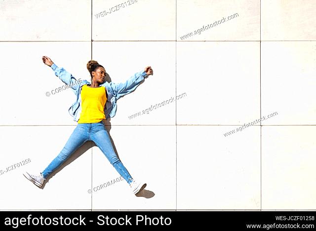 Carefree woman with arms outstretched lying on floor at sunny day