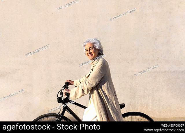 Smiling mature woman on bicycle by wall