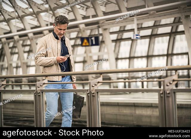 Mature businessman using smart phone walking with bag at railroad station