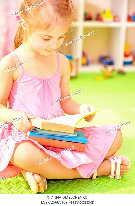 Cute little schoolgirl sitting at home on the floor with books and preparing to go to first class, doing homework, back to school