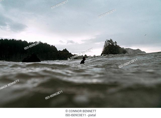 Young male surfer in cold pacific ocean, surface level view, Arcata, California, United States