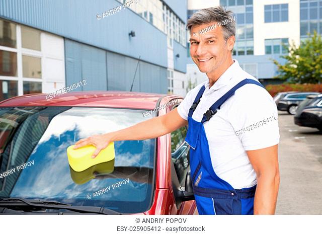 Portrait of happy male worker cleaning car windshield with sponge
