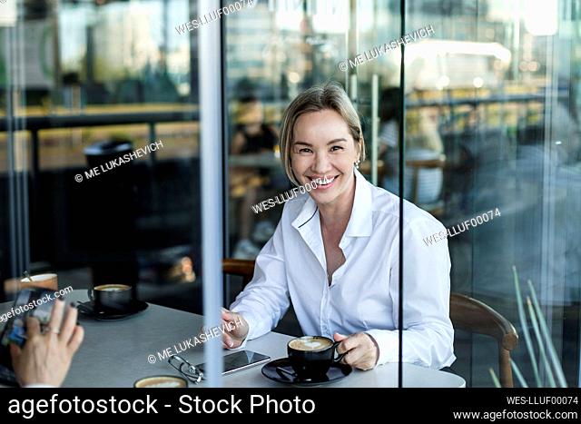 Smiling businesswoman having coffee with coworker at cafe