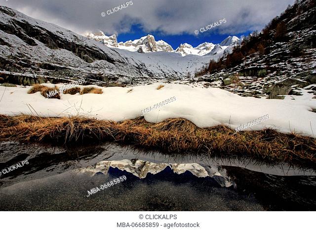 Pizzo Cengalo and Gemelli are reflected in a pool clear of snow in Val Porcellizzo. Valmasino Valtellina. Lombardy Italy Europe