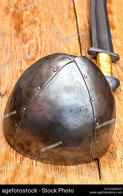iron steel helmet stands on the background of a long sword on a wooden table