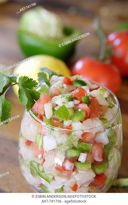 Close-up of large glass filled with Ceviche. Lemon, pepper & tomatoes in background