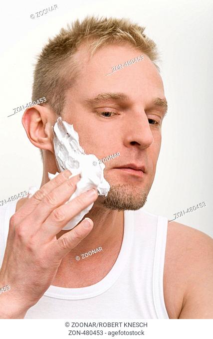 Blonder Mann cremt sein Gesicht mit Rasierschaum ein