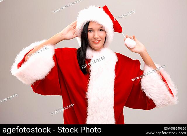 Cheerful young woman wearing huge Santa Claus costume, looking at camera, isolated on gray background